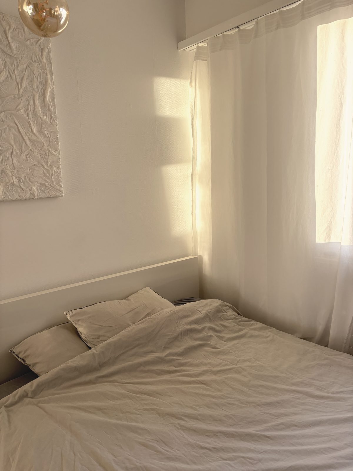 A calm bedroom with linen bedding and morning light through a sheer curtain